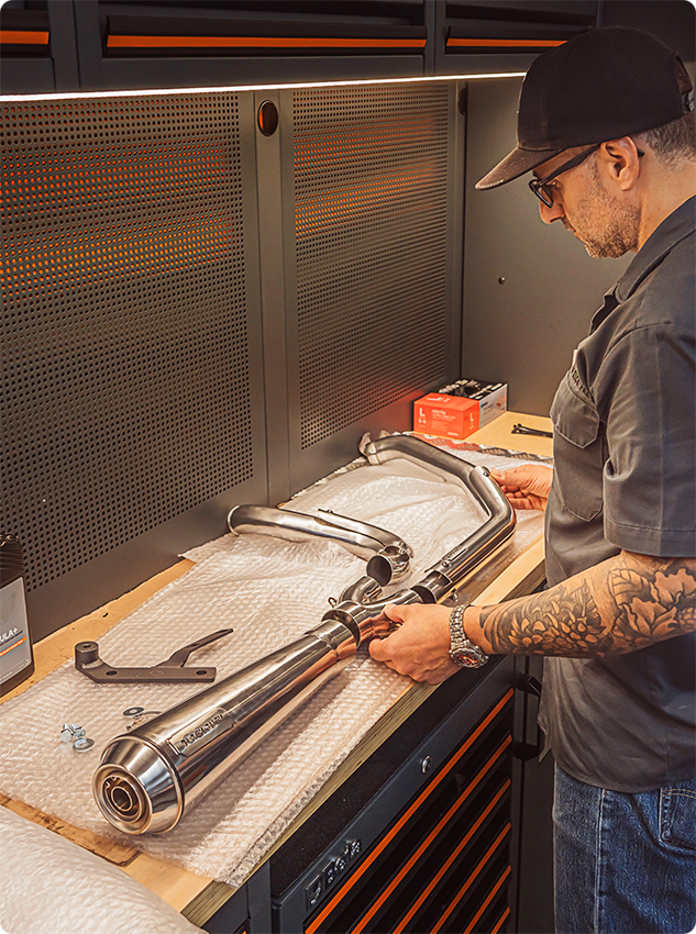 Black Duck Fighter exhausts for Softail and Touring Bagger on a table with worker inspecting, CE approved and lifetime warranty